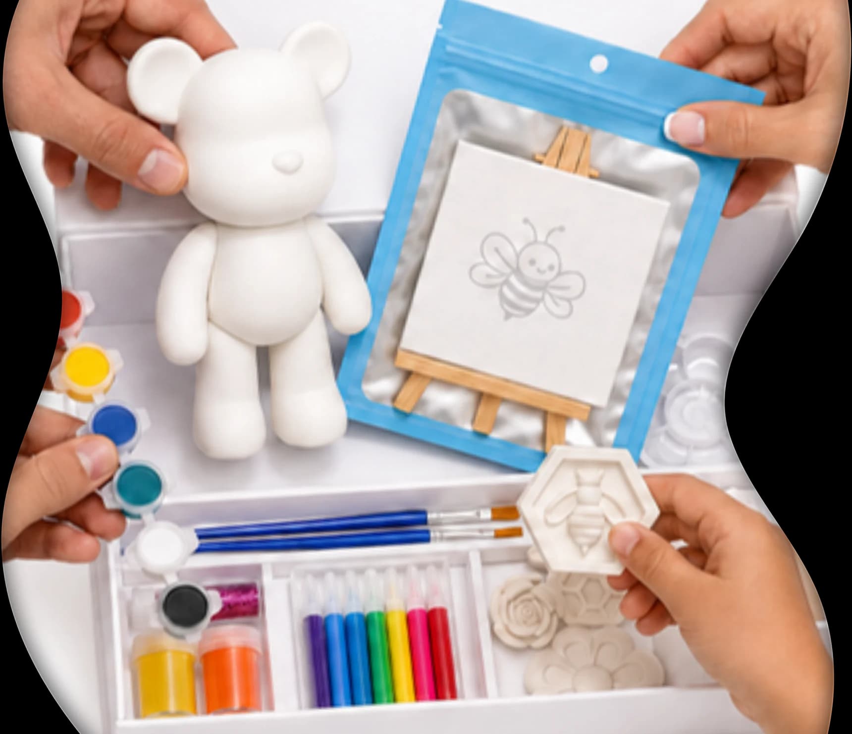 Four hands opening a Blueby kit: the plaster bear, the mini canvas, the paint pots and the brushes