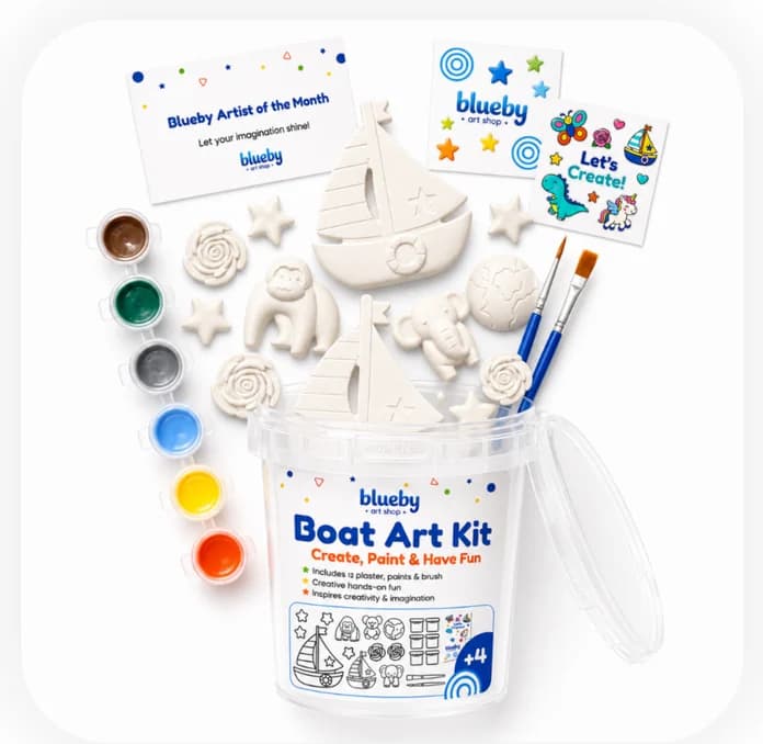 A Boat Art Kit bucket with plaster figurines, paint pots, brushes, a sticker sheet and a certificate laid out around it